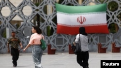 Disa gra iraniane shihen duke kaluar pranë një rruge në Teheran ku është vendosur flamuri i Iranit. 27 prill 2026.