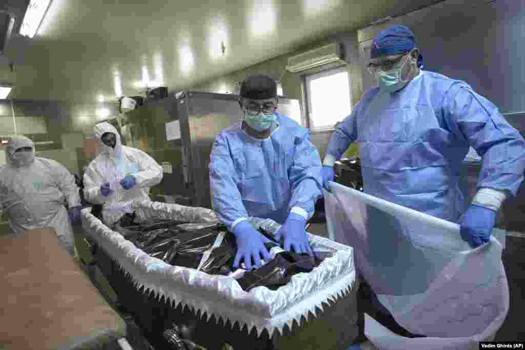 Medical staff and funeral home employees place the body of a COVID-19 victim in a coffin at a hospital morgue in the Romanian capital, Bucharest.&nbsp;