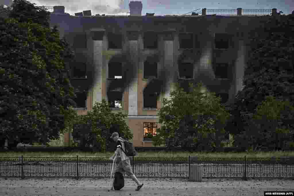 A man on crutches walks past a burning building after a strike in the city of Lysychansk in eastern Ukraine.