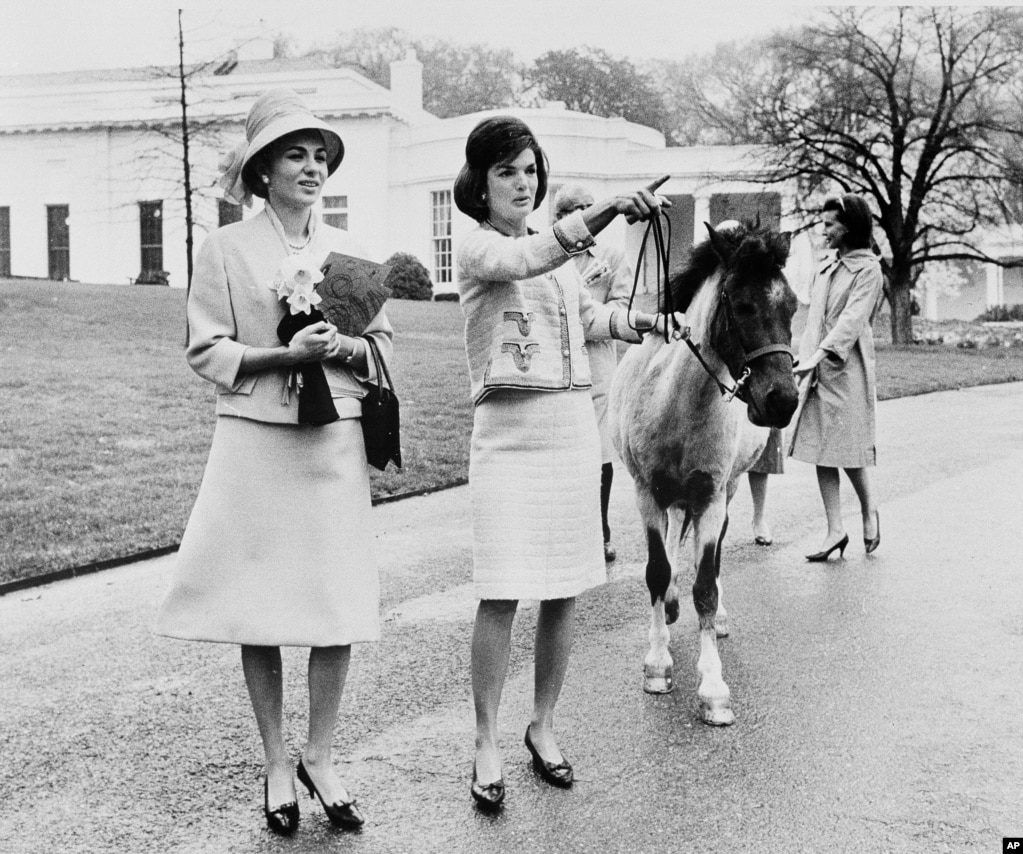 La first lady americana Jacqueline Kennedy offre una visita guidata ai giardini della Casa Bianca all'imperatrice Farah a Washington nell'aprile 1962. Kennedy guida il pony di sua figlia Caroline, Macaroni, che aveva annusato l'imperatrice, attratto dai narcisi che portava con sé .  Sullo sfondo c'è l'addetta stampa della first lady, Pamela Turnure. 