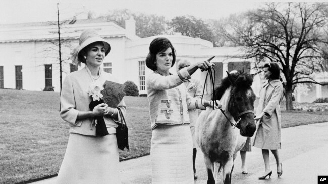 Në këtë fotografi të 12 prillit 1962, zonja e parë amerikane Jacqueline Kennedy i bën një turne udhërrëfyes në ambientet e Shtëpisë së Bardhë perandoreshës Farah Pahlavi të Iranit.