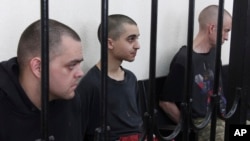 British citizens Aiden Aslin (left) and Shaun Pinner (right) and Moroccan Saaudun Brahim sit behind bars in a courtroom in Donetsk on June 9.