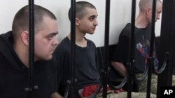 Aiden Aslin (left), Saaudun Brahim (center), and Shaun Pinner sit behind bars in a courtroom in Donetsk on June 9.