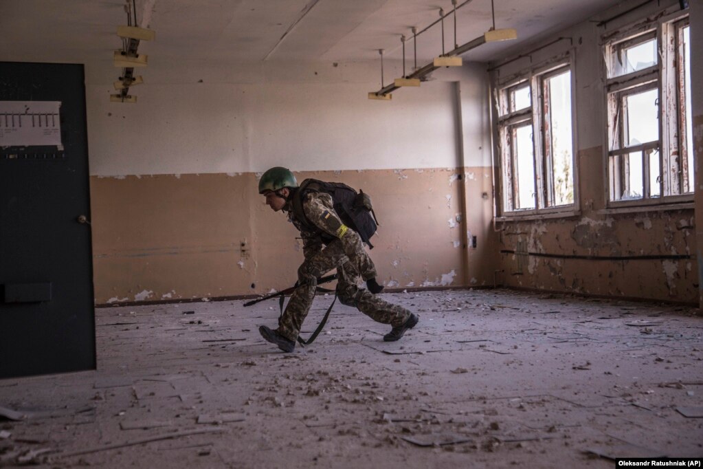 Një ushtar ukrainas vrapon i përkulur për t'u mbrojtur.