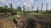 Украински војник стои во кратер од гранати до уништени руски воени возила на поле во близина на јужниот град Миколајев на 12 јуни