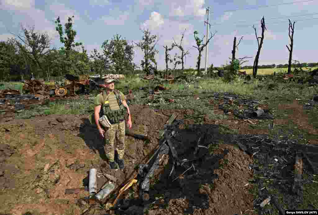 A Ukrainian soldier stands in a shell crater next to destroyed Russian military vehicles in a field near the southern city of Mykolayiv on June 12. The region is strategically important as Mykolayiv, located on the Black Sea coast, stands in the way of Russian forces trying to reach the larger port of Odesa.