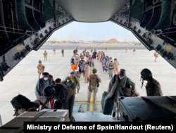 Испанские солдаты помогают афганским беженцам садиться в военно-транспортный самолет. Аэропорт Кабула, 22 августа 2021 года
