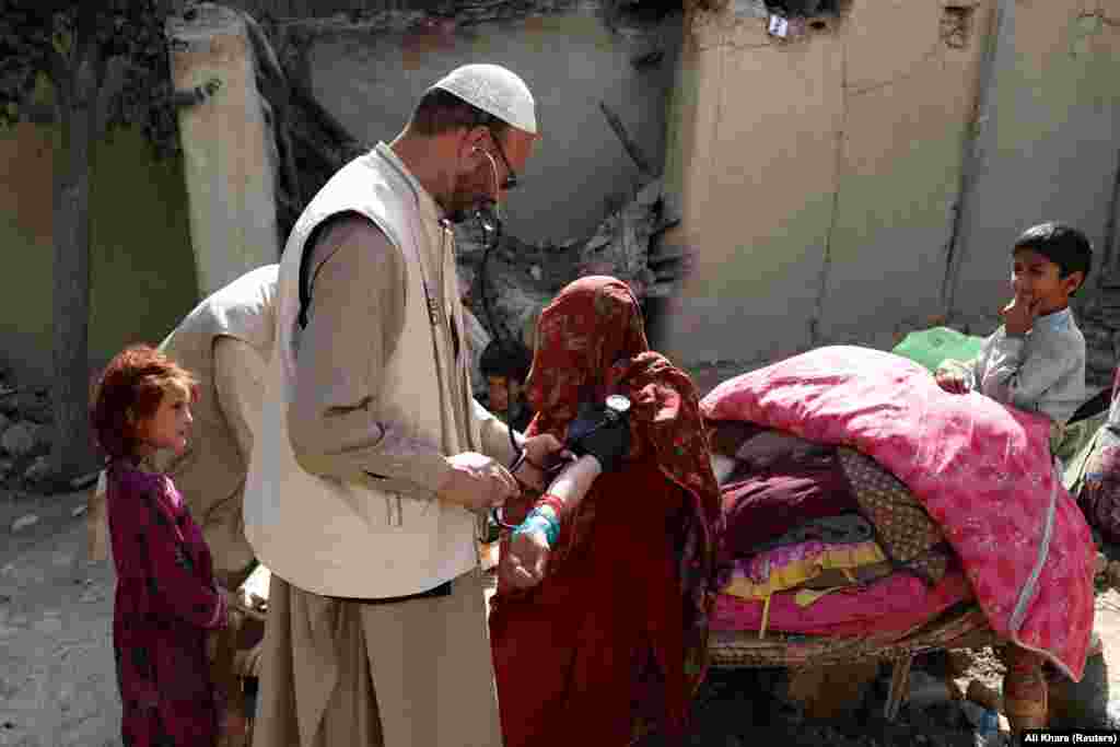 Children look on as an Afghan doctor treats an injured woman.