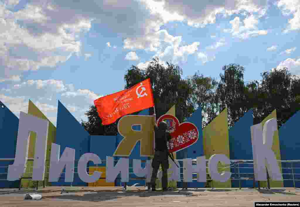 Поддерживаемый Россией сепаратист держит флаг советских времен у композиции &laquo;Я люблю Лисичанск&raquo; после того, как украинские войска оставили город. 4 июля 2022 года