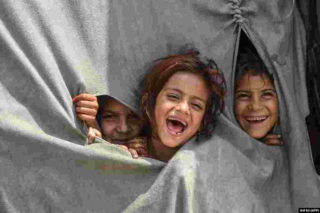 Children of Afghan refugees living in Pakistan smile for the camera from inside their makeshift tent on the outskirts of Lahore on June 19.