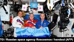 În această fotografie difuzată de agenția spațială rusă Roscosmos pe 4 iulie 2022, cosmonauții ruși Oleg Artemyev (centru), Denis Matveyev (dreapta) și Sergei Korsakov pozează cu steagul autoproclamatei Republici Populare Lugansk la bordul Stației Spațiale Internaționale