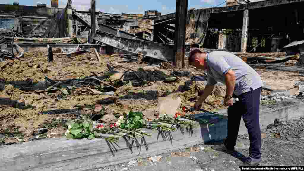 Чоловік покладає квіти біля уламків зруйнованого ТРЦ &laquo;Амстор&raquo; у Кременчуці