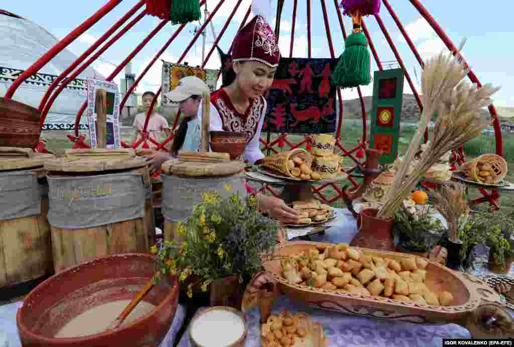A traditionally dressed Kyrgyz girl sells tasty treats to visitors while surrounded by colorful tapestries evoking the richness of her unique culture.