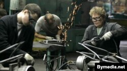 Жанчына працуе поруч з мужчынамі на роварным заводзе.