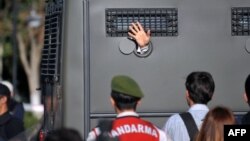 An Ergenekon prisoner being driven in a police armoured vehicle waves at protesters in August 2013 as police and gendarmerie block access to a courthouse in Silivri, near Istanbul.