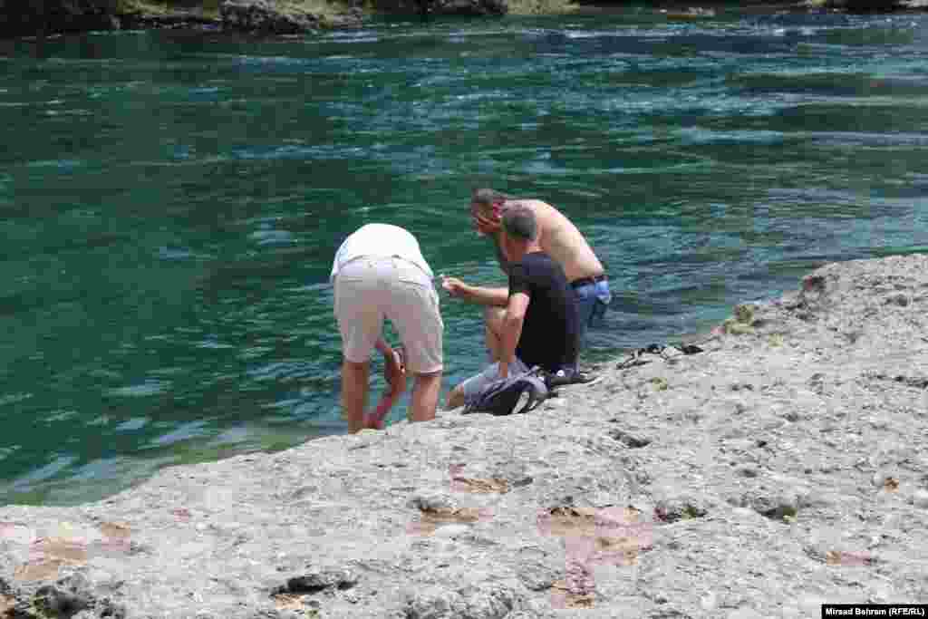 Troje turista na obali rijeke Neretve, ispod Starog mosta u Mostaru, nastoje se rashladiti od nesnosnih vrućina.