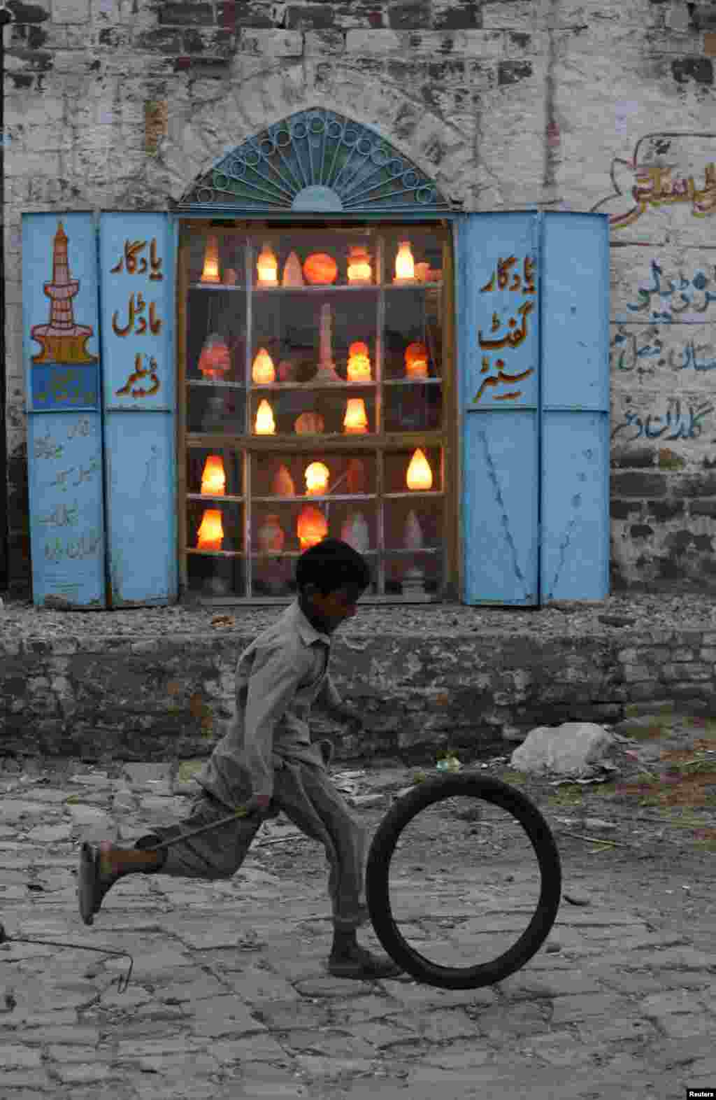 A Pakistani boy runs past a shop selling lamps and decoration pieces.&nbsp;