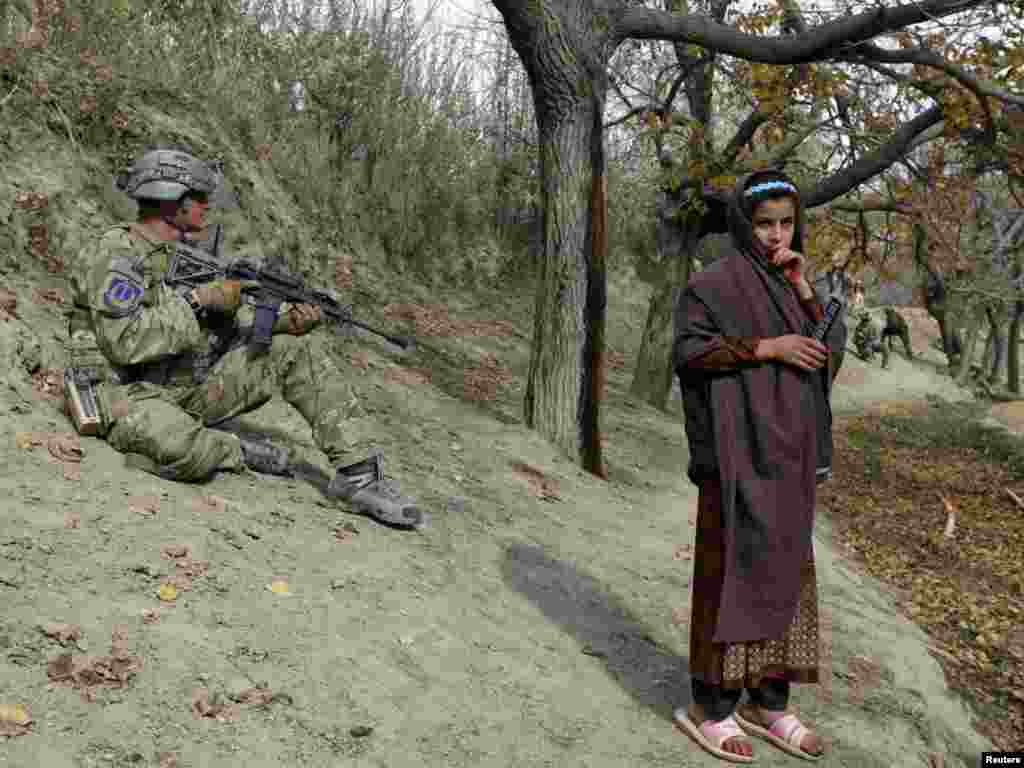 A U.S. soldier takes position as an Afghan girl stands next to him during a patrol as part of an overall security and disruption insurgency mission in Wardak Province on November 17. (REUTERS/Umit Bektas)