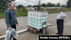 Localnici veniți să își alimenteze bidoanele cu apă de la un recipient public, într-un cartier din Târnăveni.