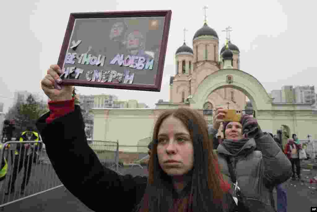 A fotón egy fiatal nő tart a kezében egy fotót Navalnijról és özvegyéről, Julija Navalnajáról: &bdquo;Az örök szerelem nem ismeri a halált&rdquo;