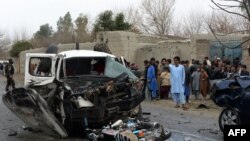 Bystanders look on as security force personnel inspect wreckage of vehicles at the site of a roadside rickshaw bomb explosion that targeted a senior local police vehicle in Behsood District of Nangarhar province on February 28.