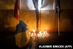 A woman draped in a Ukrainian flag lights a candle on October 1 at a memorial for slain investigative journalist Jan Kuciak and his fiancee, Martina Kusnirova, in reaction to the results of the elections in Bratislava.
