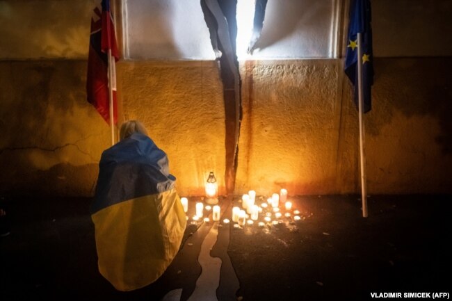 Una donna avvolta in una bandiera ucraina accende una candela in memoria dei giornalisti investigativi Jan Kuciak e Martina Kusnirova uccisi in reazione ai risultati delle elezioni a Bratislava il 1° ottobre.