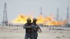 Flames burn off excess gas behind policemen standing guard at Zubair oil field in Iraq's southern province of Al-Basrah in late June.