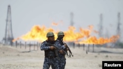 Flames burn off excess gas behind policemen standing guard at Zubair oil field in Iraq's southern province of Al-Basrah in late June.