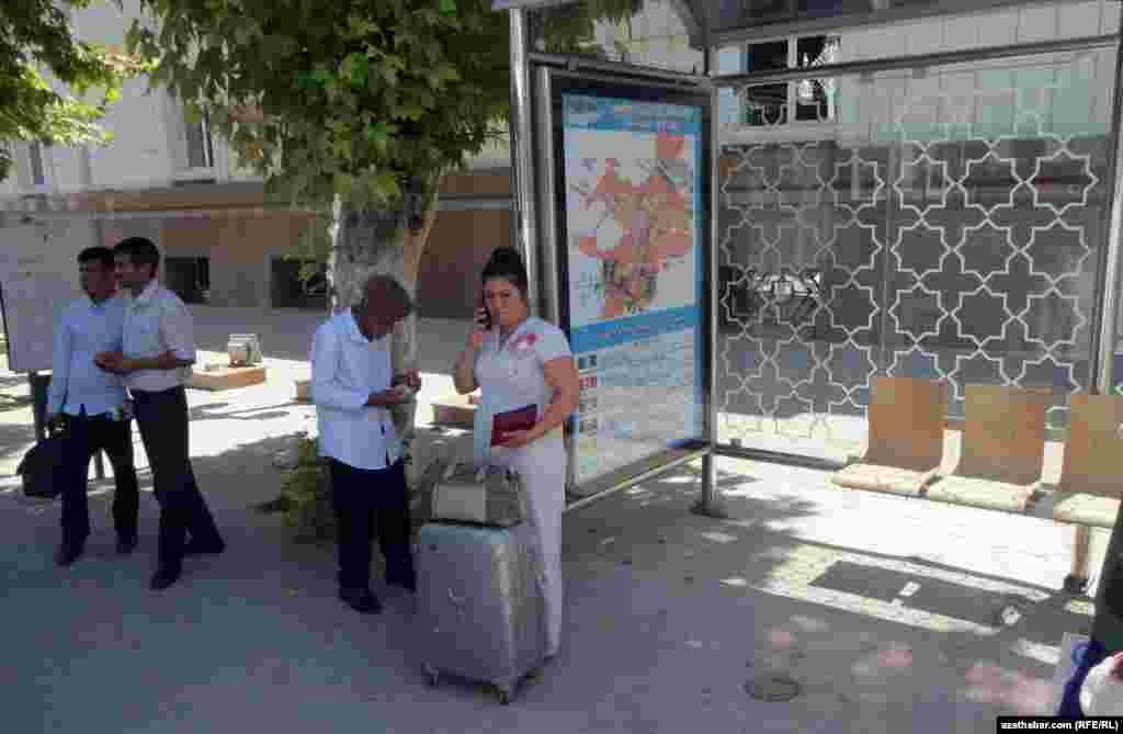 Duralgada awtobusa garaşyp duran eli çemodanly bir ýolagçy.