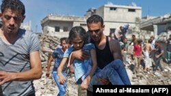 SYRIA -- A man carries a child rescued from rubble after Syrian regime and Russian air strikes in the rebel-held town of Nawa, about 30 kilometres north of Daraa in southern Syria on June 26, 2018.