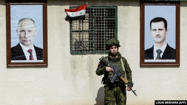 A Russian military man stands between portraits of Syrian President Bashar al-Assad (right) and Russian President Vladimir Putin at a checkpoint on the outskirts of Damascus, March 1, 2018.