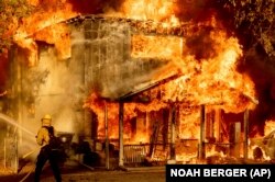 Egy tűzoltó vizet permetez, miközben megpróbálja megakadályozni, hogy a tűz átterjedjen a szomszédos házakra a kaliforniai Doyle-ban. Képünk illusztráció
