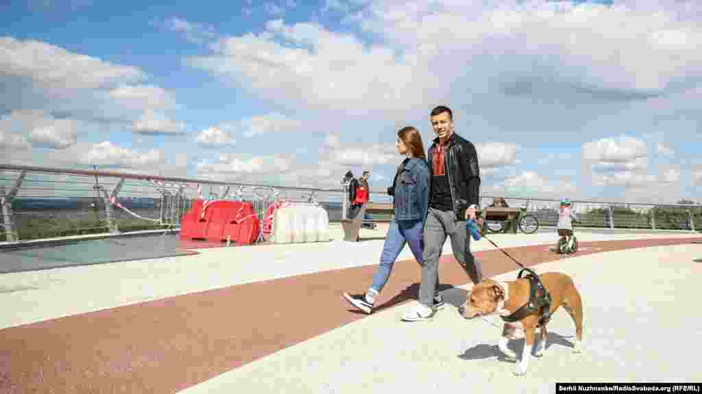 Пара с собакой прогуливается по пешеходному мосту&nbsp;