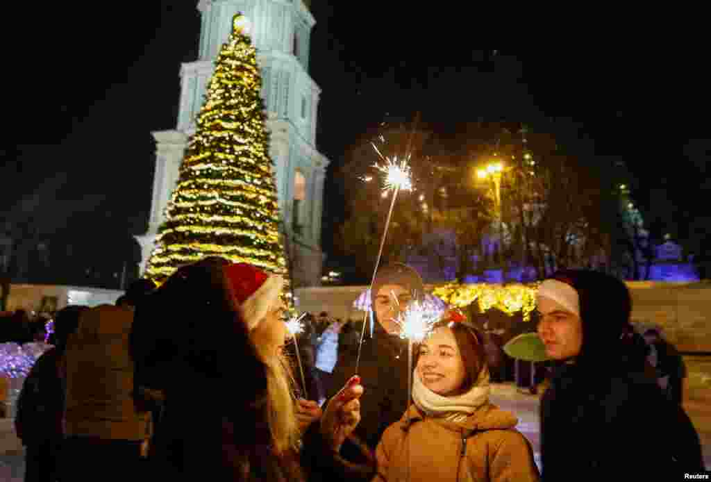 Oamenii cu artificii stau lângă un brad de Crăciun în timpul sărbătoririi Revelionului, înainte de închiderea traficului, pe fondul atacului Rusiei asupra Ucrainei, la Kiev, Ucraina, 31 decembrie 2025. Foto REUTERS/Gleb Garanich