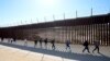 Një grup njerëzish duke ecur përgjatë murit, pasi e kanë kaluar kufirin me Meksikën për të kërkuar azil në Shtetet e Bashkuara, 24 tetor 2023.