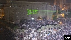 محتجون يتجمعون في ميدان التحرير بالقاهرة، فيما تظهر كلمة (مصر) بالإنكليزية مكتوبة بأشعة الليزر على بناية مجمع الدوائر الحكومية. 