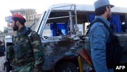 Afghan National Army (ANA) soldiers and Afghan police stand next to a damaged military bus following an explosion in western Kabul on October 21, 2014.