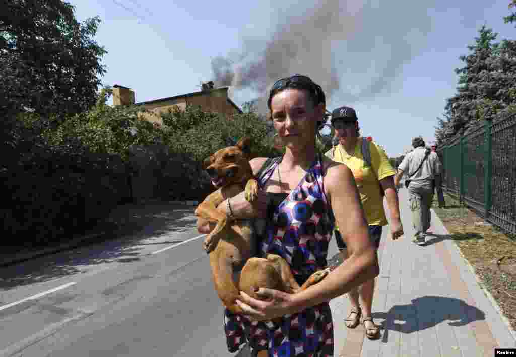 A woman carries a dog as smokes rises above buildings shortly after a shelling in Donetsk in August 2014.