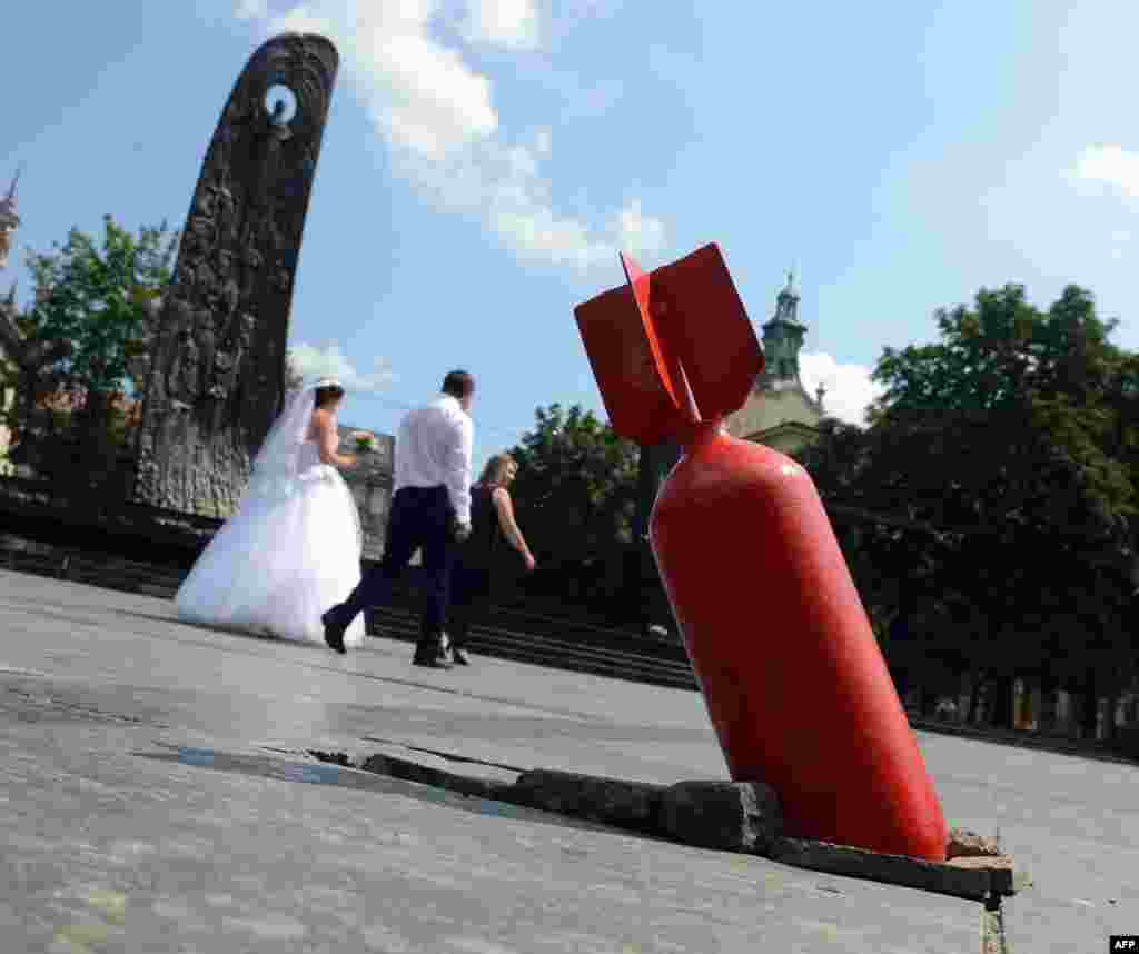 A newly married couple walks past an art installation showing an unexploded bomb, set near the Taras Shevchenko monument (left) in the center of the western Ukrainian city of Lviv, close to Poland&#39;s border. (AFP/Yurko Dyachyshyn)