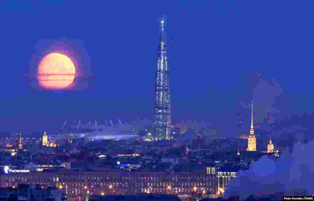 A full moon sliding behind the tower on March 28. At right is the golden spire of St. Petersburg&#39;s Peter and Paul Cathedral.