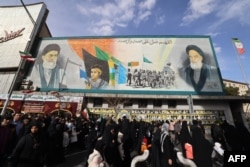 Люди на площади Энгелаб (Исламской Революции) в Тегеране проходят мимо транспаранта с изображением Высшего руководителя великого аятоллы Али Хаменеи и покойного Высшего руководителя великого аятоллы Рухоллы Хомейни. 14 января 2026 года