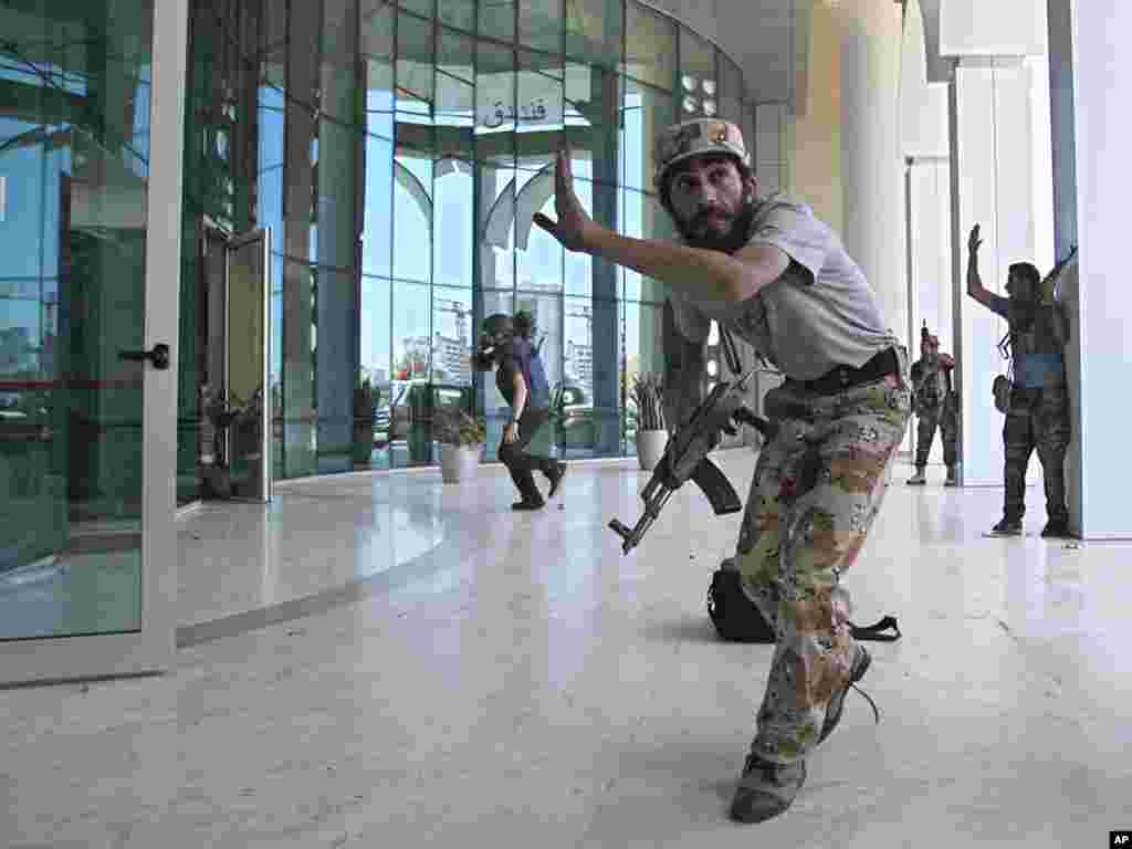 Libyan rebel fighters and a television cameraman take shelter as an intense gun battle erupted outside the Corinthia Hotel, where many foreign journalists stayed.