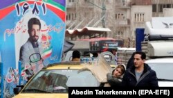 A couple walks past an electoral billboard in a street in Tehran, February 17, 2020