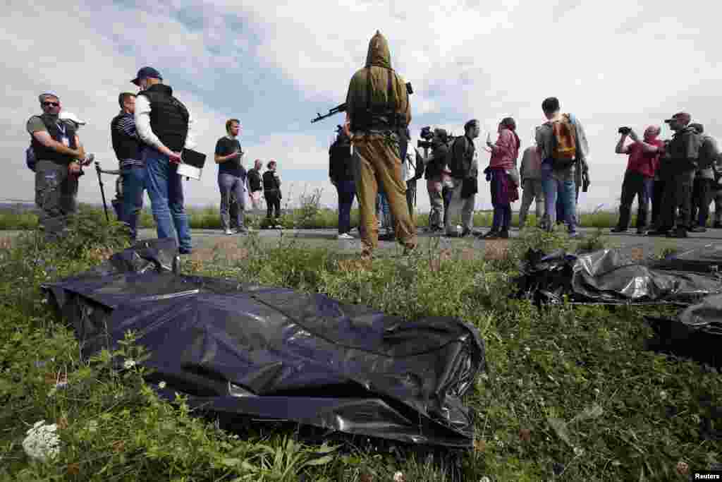 OSCE monitors and journalists look on as a pro-Russian separatist stands guard near bodies taken from a crash site.&nbsp;