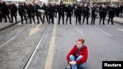 An antigovernment protester sits on the ground in front of police during a demonstration in Sarajevo.