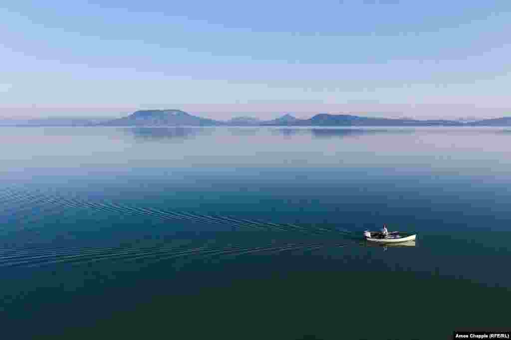 A fisherman motors along Lake Balaton on a perfectly still summer morning. The lake runs for nearly 80 kilometers and is 14 kilometers across at its widest point, making it the largest lake in Central Europe. It is also one of the shallowest, with most &ldquo;swimmers&rdquo; needing to wade out hundreds of meters to reach waist-deep water.