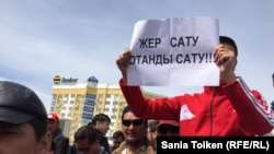 Участник протеста в Атырау держит плакат: "Продать землю — значить продать родину". 24 апреля 2016 года.
