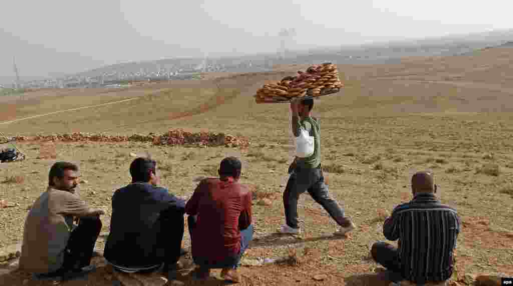 A vendor sells simit, a&nbsp;Turkish traditional food,&nbsp;as people watch on a hill during armed clashes between YPG Kurdish fighters and Islamic State fighters in Kobani, Syria, near Suruc district, Sanliurfa, Turkey. (EPA/Tolga Bozoglu) 