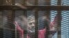 EGYPT -- Egyptian ousted Islamist president Muhammad Morsi, wearing a red uniform, gestures from behind the bars during his trial in Cairo at the police academy, April 23, 2016